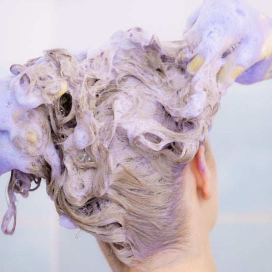 Blonde hair being cleansed with a purple-toned lather designed for a platinum haircare routine.