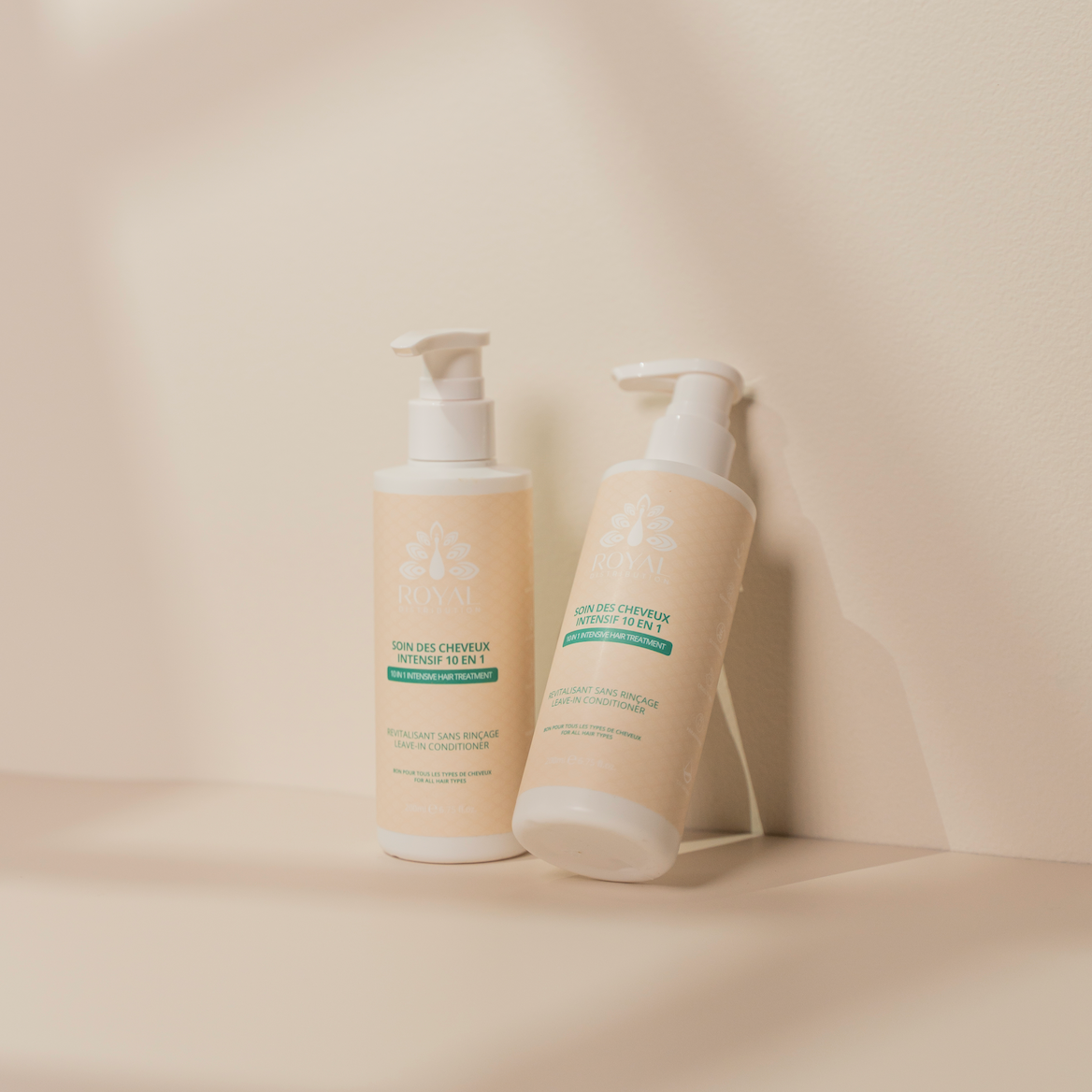 Two ROYAL 10 in 1 Leave-In Conditioner bottles styled against a minimalist warm beige background with soft natural shadows.