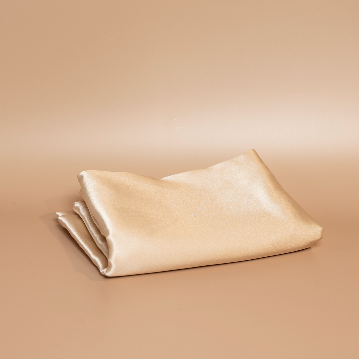 Folded beige ROYAL silk satin pillowcase photographed against a beige background.