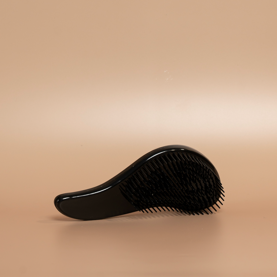 Black ROYAL detangling hair brush photographed against a beige background.