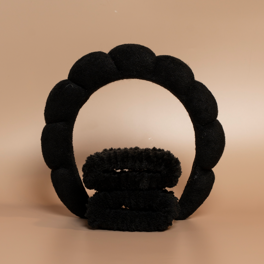 Black ROYAL hair care headband and matching fabric wristbands displayed together against a beige background.