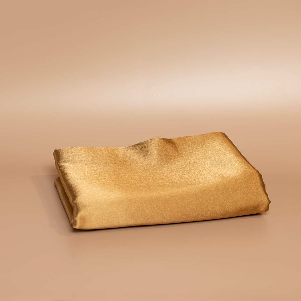 Folded caramel ROYAL silk satin pillowcase photographed against a beige background.