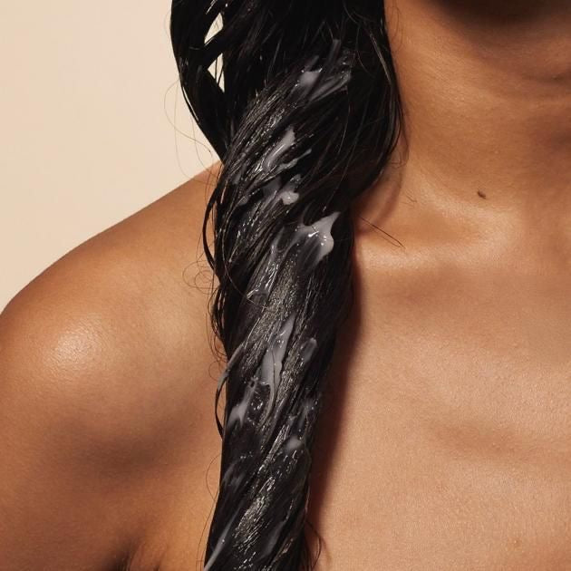 Close-up of a dark, wet hair strand coated with white cream, resting against a woman's shoulder.