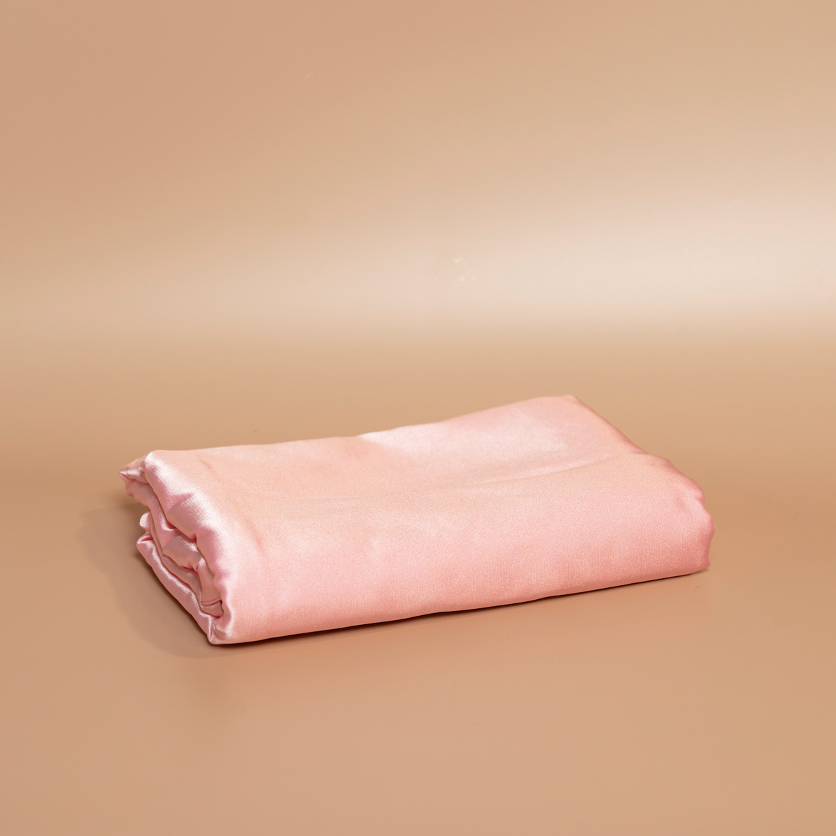 Folded deep pink ROYAL silk satin pillowcase photographed against a beige background.