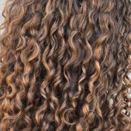 Close-up of defined brown curls with dimensional highlights and a naturally textured finish.