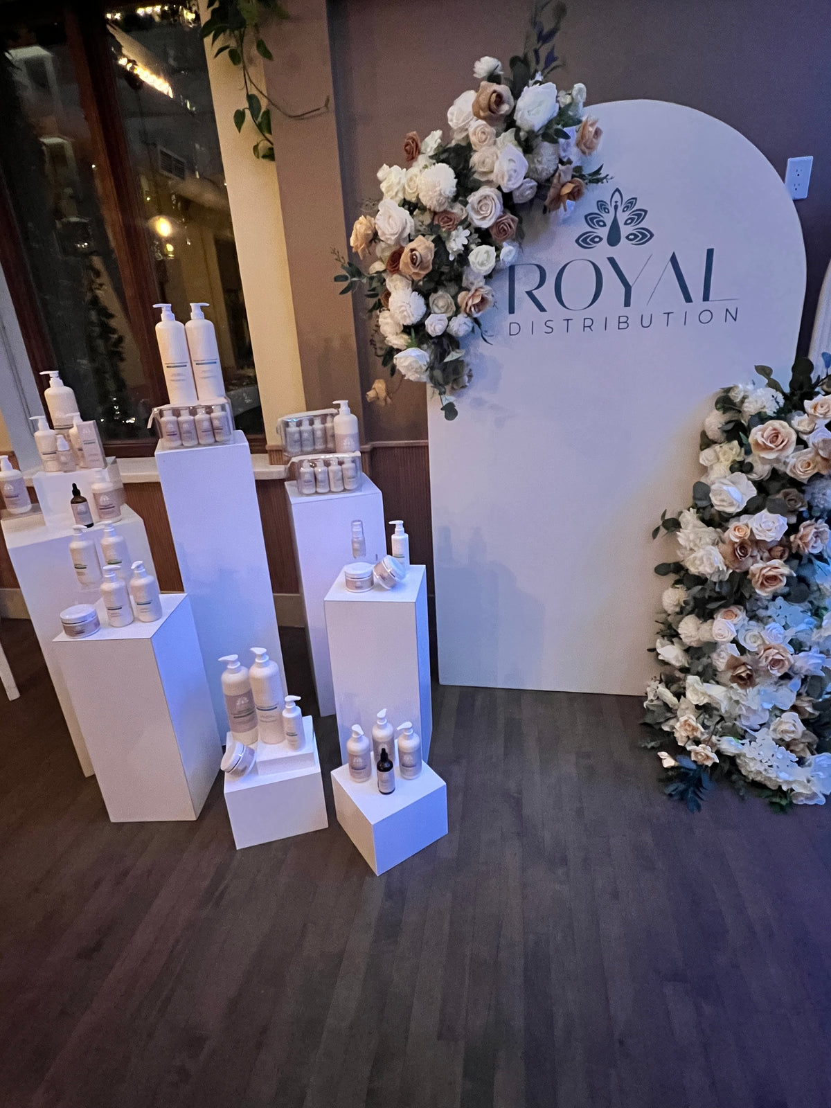 ROYAL haircare collection arranged on white display pedestals beside a floral ROYAL Distribution backdrop.