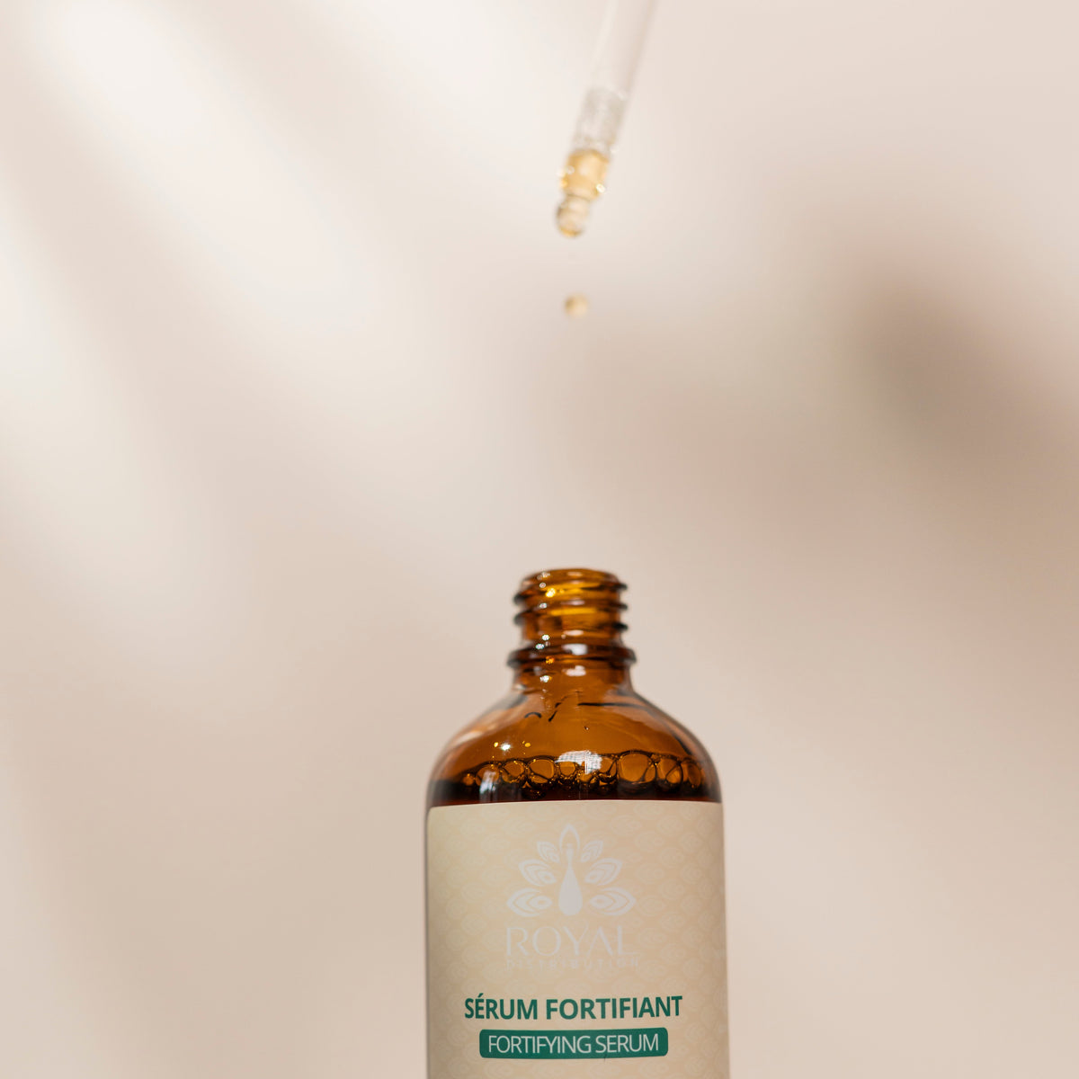 Close-up of ROYAL Fortifying Serum in an amber glass bottle as a drop of serum falls from a glass dropper above it.