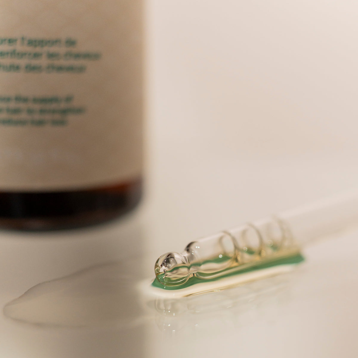 Close-up of the clear lightweight texture of ROYAL Fortifying Serum displayed beside its amber glass bottle on a neutral surface.