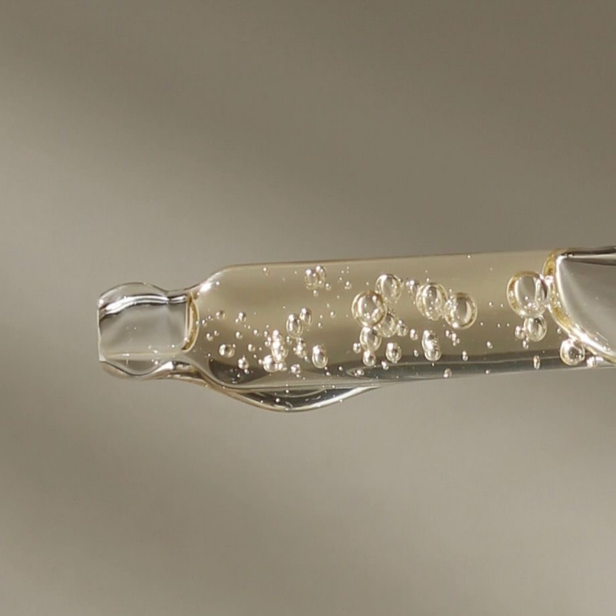 Close-up of a clear hair care formula with visible air bubbles on a glass applicator.