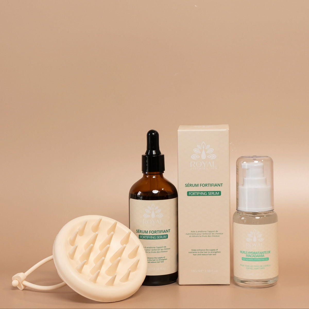 ROYAL hair care kit featuring the Fortifying Serum, Macadamia Hydrating Oil, and a cream-colored silicone scalp massage brush, arranged on a warm beige background.