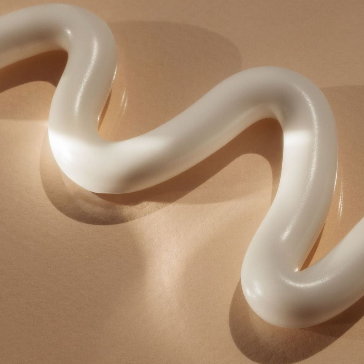Close-up of a smooth white cream texture arranged in a flowing shape on a warm beige background.