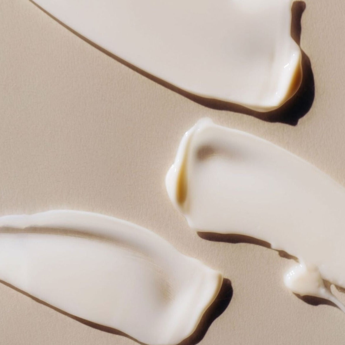 Close-up of a rich white cream formula spread across a neutral beige surface.