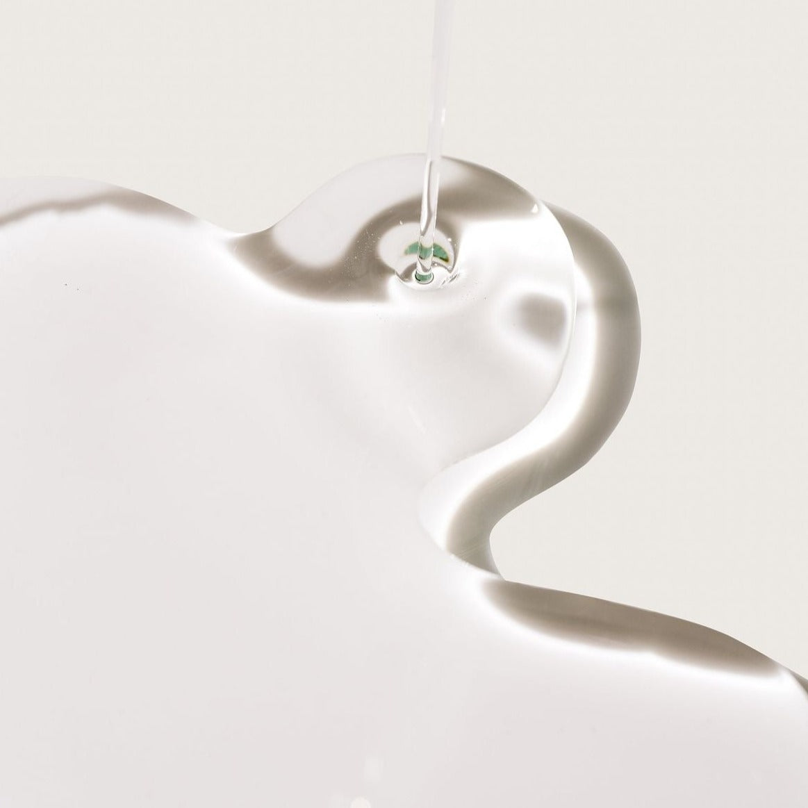 Close-up of the clear and glossy texture of ROYAL Hydrating Macadamia Oil flowing across a light neutral surface.
