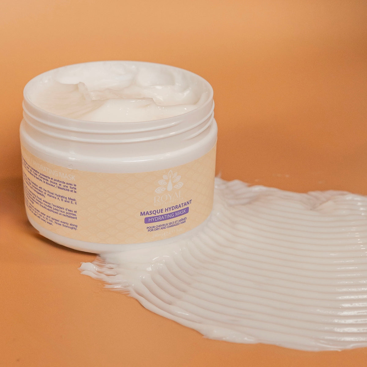 Open jar of ROYAL Hydrating Mask with its rich creamy texture displayed across a warm beige studio surface.