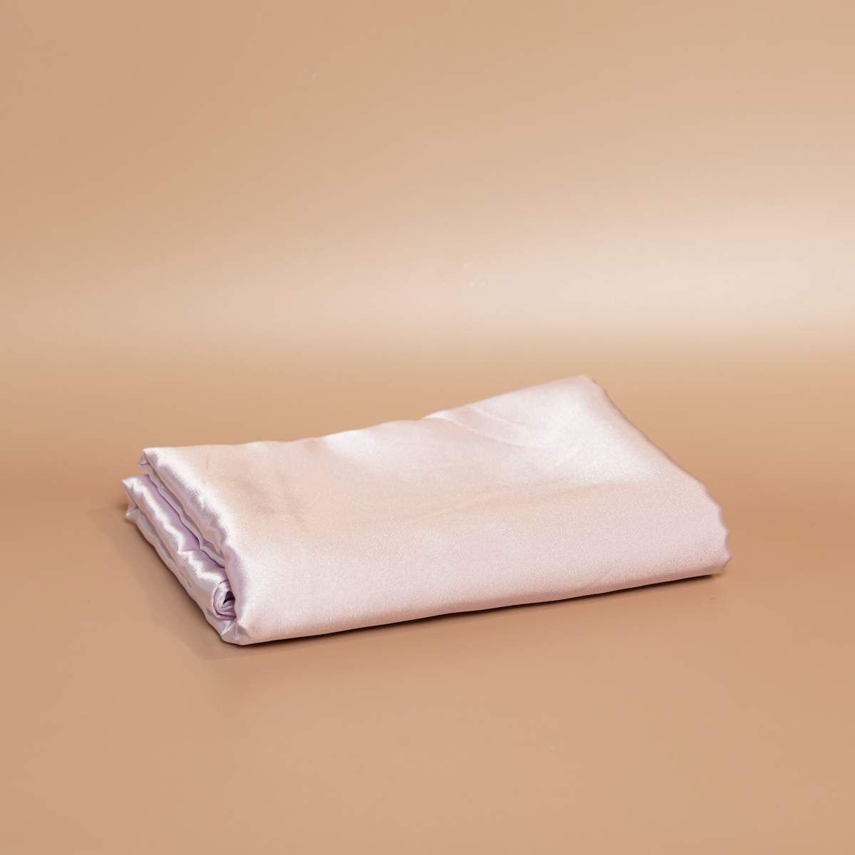 Folded lilac ROYAL silk satin pillowcase photographed against a beige background.