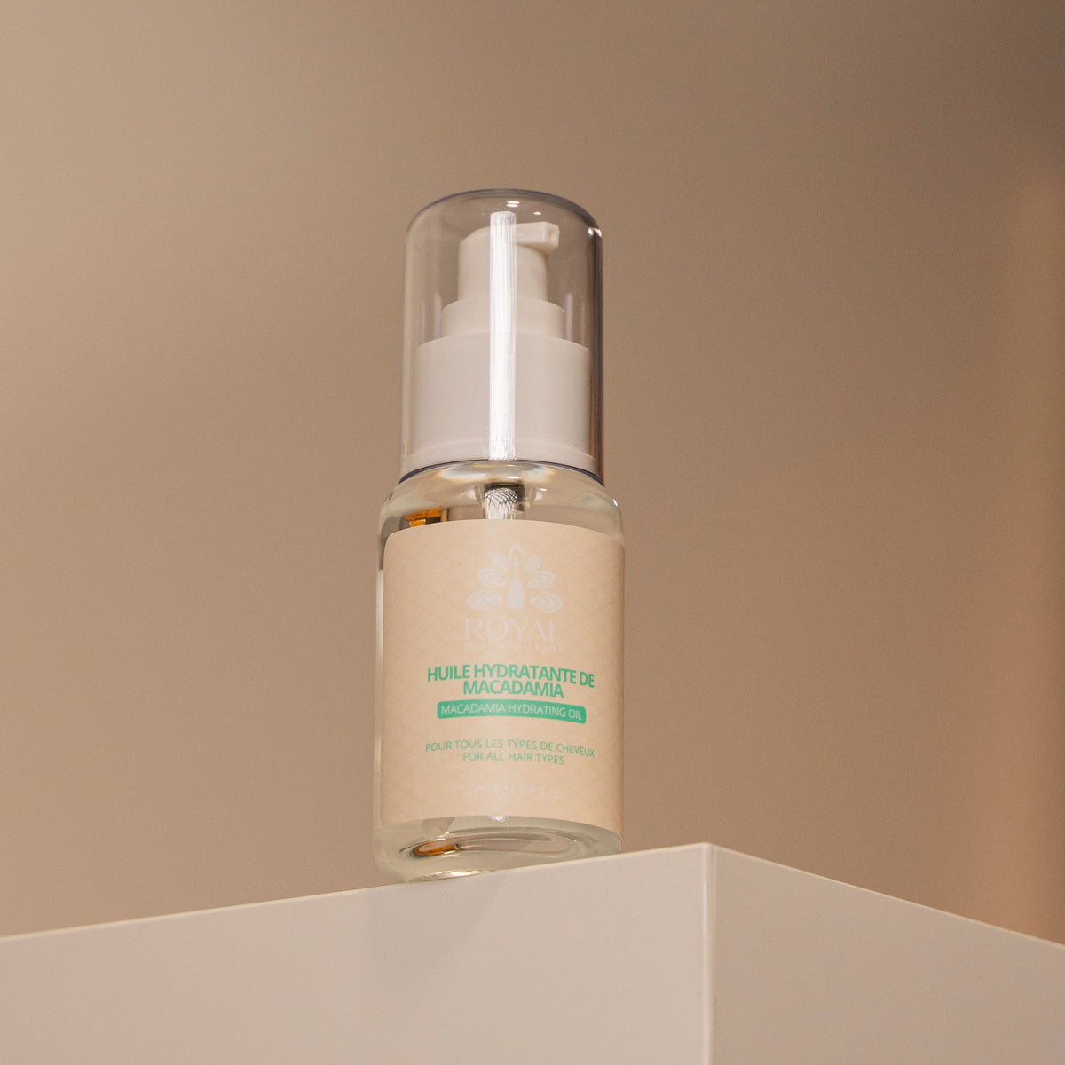 ROYAL Macadamia Hydrating Oil bottle displayed on a minimalist pedestal against a warm neutral background.