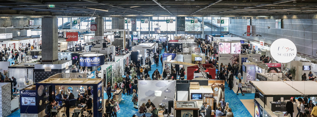 Professional beauty industry event featuring exhibitors, brands and attendees in a large exhibition hall.