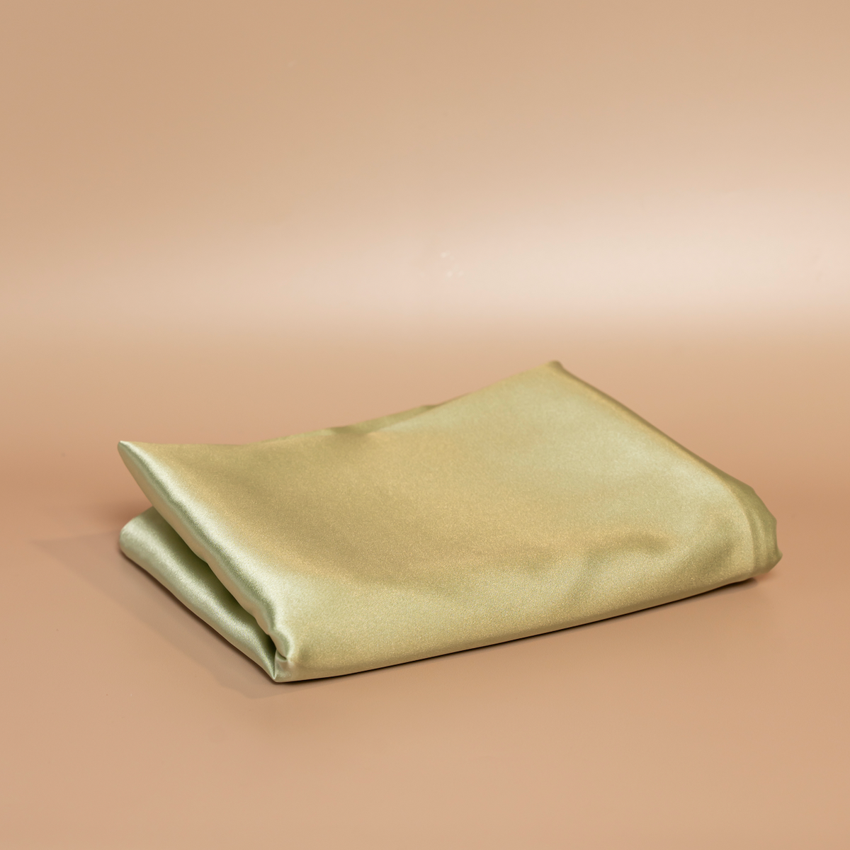 Folded sage green ROYAL silk satin pillowcase photographed against a beige background.