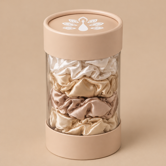 ROYAL satin hair scrunchies in elegant ivory, champagne, soft gold and blush beige shades, beautifully displayed in a clear cylindrical packaging with a nude beige lid and signature ROYAL logo.