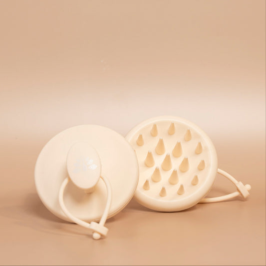 Close-up of the beige ROYAL scalp massage brush, showing its rounded shape and flexible silicone bristles.