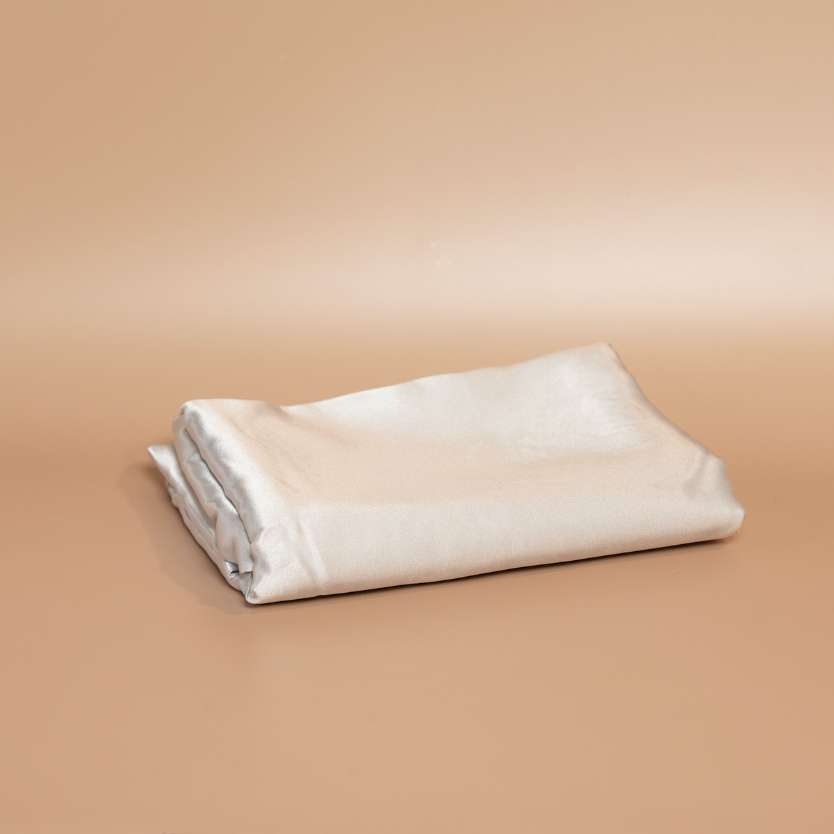 Folded silver ROYAL silk satin pillowcase photographed against a beige background.