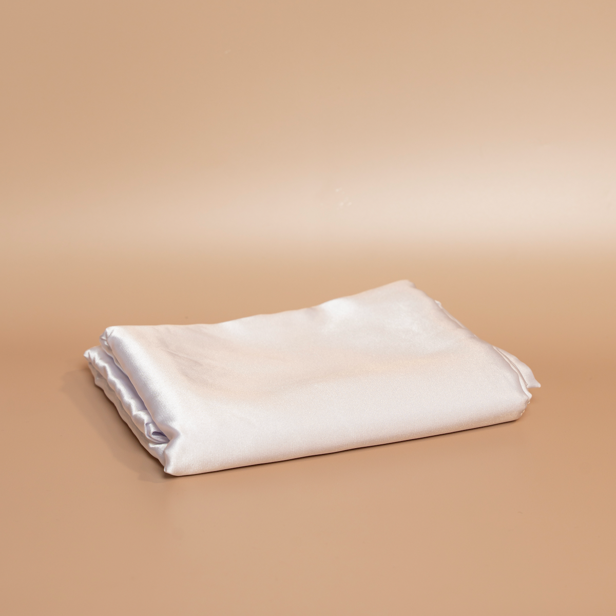 Folded white ROYAL silk satin pillowcase photographed against a beige background.